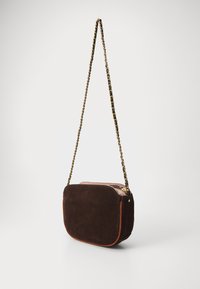 Borsa a tracolla in suede marrone con bordi in pelle arancione e tracolla in catena dorata. Presenta una chiusura con zip e una forma arrotondata.