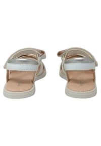 Sandali bianchi con cinturino argento, soletta imbottita morbida, cinturino posteriore regolabile e suola in gomma. Presentano un design minimalista.