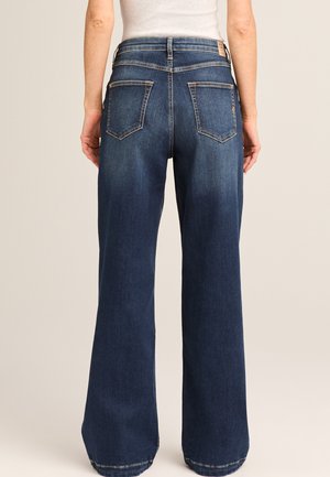 Back view of a person wearing high-waisted, dark blue wide-leg jeans with back pockets and a white top.