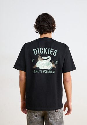 Camiseta de algodón negra con un gráfico de serpiente y el texto "DICKIES 1922 QUALITY WORKWEAR" en la parte posterior. Mangas cortas, corte relajado.