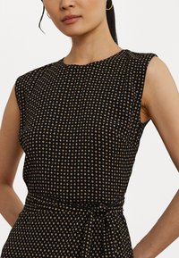 Black dress featuring a dotted pattern in gold. It has cap sleeves, a round neckline, and a tied waist detail for a fitted silhouette.