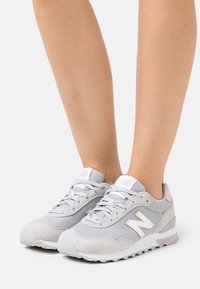 Gray athletic shoes with mesh and suede material. Features a white logo, light pink accents, and a textured sole for grip and support.