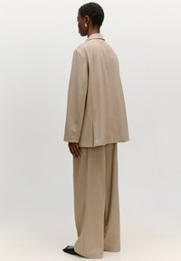 Beige op maat gemaakt kostuum met een losse jas en brede broek, met een gladde stofstructuur en subtiele stikdetails.