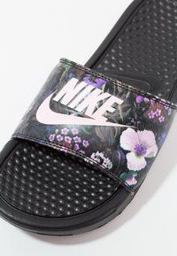 Sandale slide noire Nike avec semelle texturée et bride fleurie comportant un logo Nike blanc et un swoosh.