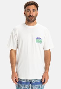 Camiseta blanca de mangas cortas confeccionada en una tela suave, con un logotipo colorido de Quiksilver en el lado izquierdo del pecho. Corte relajado y cuello redondo.