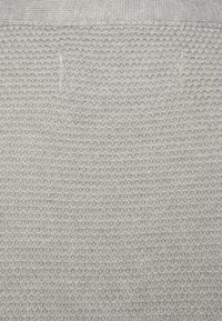 Beige stickad tyg som visar ett tryck med siffror och bokstäver i ett rutmönster i det övre vänstra hörnet.