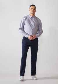 Camicia a quadri blu chiaro con colletto button-down, abbinata a pantaloni navy scuri e sneakers bianche. Tessuto liscio, design aderente.