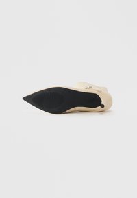 Beige pointed-toe ankle boot lying sideways, showing black rubber sole and low heel on white background.