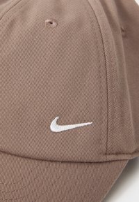 Casquette de baseball marron avec un tissu texturé, une visière courbée et un logo Nike brodé blanc à l'avant.