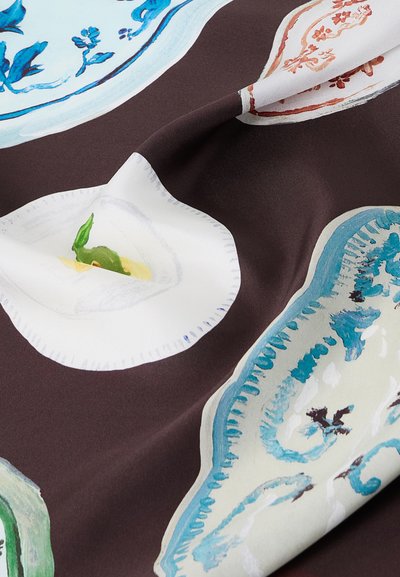 Κοντινή εικόνα υφάσματος με πολύχρωμα floral και διακοσμητικά μοτίβα πιάτων σε σκουρό καφέ φόντο, που δείχνει τις πτυχώσεις και την υφή του υφάσματος.