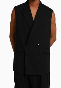 Svart ärmlös kavaj med dubbla knappar på framsidan, spetsiga slag och två sidfickor. Texturerat tyg med en slät yta.