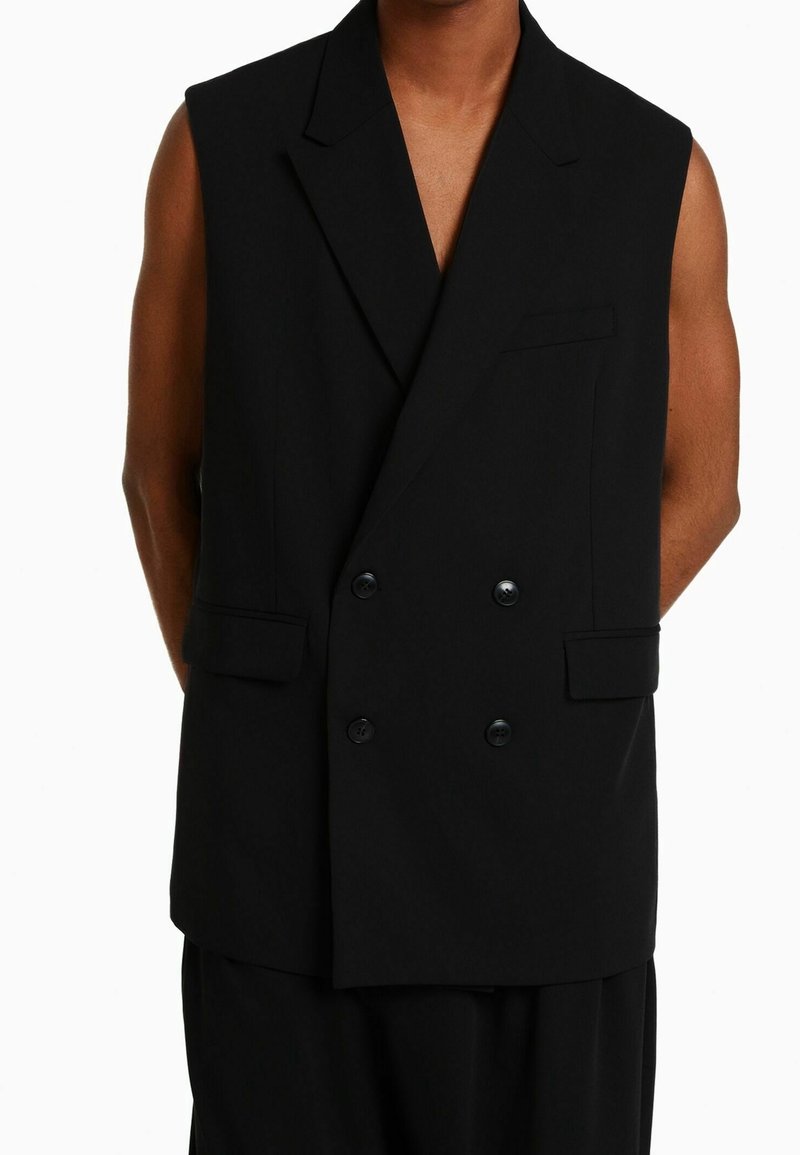 Svart ärmlös kavaj med dubbla knappar på framsidan, spetsiga slag och två sidfickor. Texturerat tyg med en slät yta.