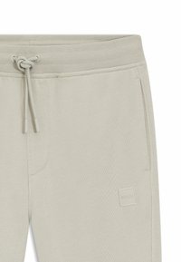 Ανοιχτό μπεζ φόρμα με κορδόνι στη μέση, πλαϊνή τσέπη και μικρό τετράγωνο λογότυπο BOSS κοντά στην τσέπη.