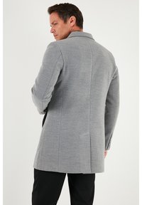 Abrigo de mezcla de lana gris con ajuste entallado, solapas con muesca y una abertura trasera única. Cuenta con mangas largas y dos bolsillos laterales.