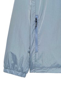 Lichtblauwe jacksleeve met elastische manchetten en een verticale ritszak aan de zijkant, gelabeld "WEEKEND".