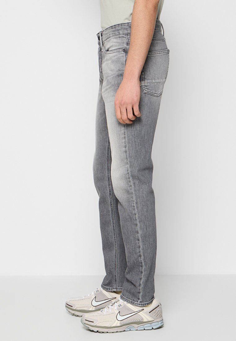 Lichtgrijze denim jeans met een rechte pijp. Heeft vijf zakken en een vervaagd uiterlijk. Draagt met crèmekleurige sneakers.