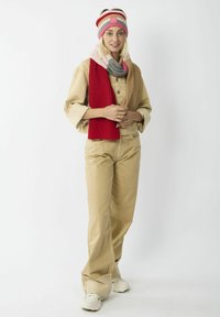 Strickmütze mit rosa, roten und grauen Streifen; rote gerippte Schal; tanfarbener Utility-Jacke; hellbeige Hose; weiße Sneakers; lässiges Outfit.