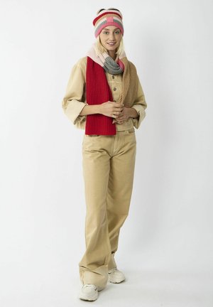 Garen muts met roze, rode en grijze strepen; rode geribbelde sjaal; tan utility jack; licht tan broek; witte sneakers; casual outfit.
