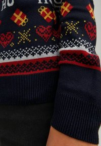 Granatowy sweter z wełny z festywnymi wzorami prezentów w czerwono-żółtych kolorach, serc i płatków śniegu. Sweter ma prążkowane mankiety i dół, a także akcentujące paski w bieli i czerwieni.
