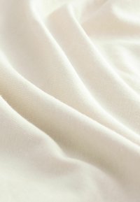 Blødt cremefarvet stof med fin tekstur og subtilt diagonalt ribmønster, draperet for at vise dets smidige kvalitet og glatte fornemmelse.