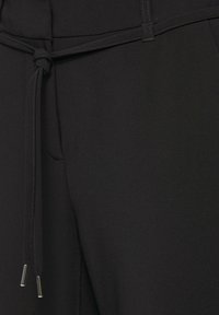 Zwarte broek met een zachte textuur, uitgerust met een gestrikt koord in de taille en zilveren hardware-accenten aan de uiteinden van de koorden.