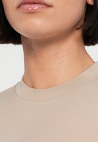 Μπεζ ριμπ πουκάμισο με στρογγυλή λαιμόκοψη, κατασκευασμένο από απαλό ύφασμα. Κοντινό πλάνο στην περιοχή του γιακά που αναδεικνύει την ομαλή υφή και τον απλό σχεδιασμό.