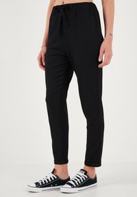Zwarte, gestructureerde joggingbroek met een elastische tailleband en strikdetail, voorzien van taps toelopende benen en opgerolde boorden, gecombineerd met navy sneakers.