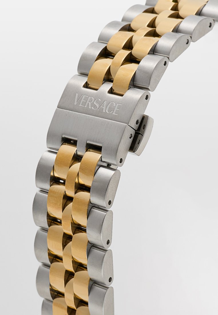 Cinturino per orologio in acciaio inox e metallo color oro, caratterizzato da collegamenti interbloccati, finitura spazzolata e un fermaglio inciso con "VERSACE."