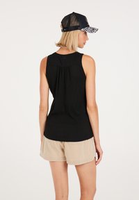 Top senza maniche nero con una finitura testurizzata, caratterizzato da un dettaglio arricciato sul retro. Abbinato a pantaloni corti in velluto a coste beige e un cappellino in rete nero.