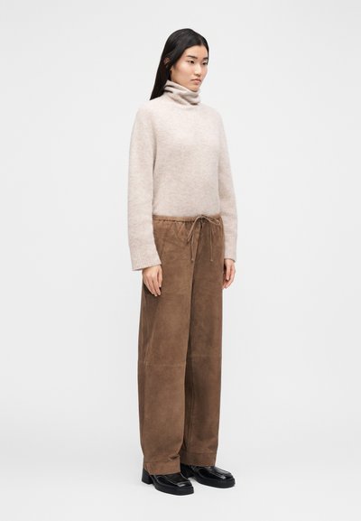 Világos bézs garbó pulóver barna velúr nadrággal, rugalmas húzózsinóros derékrésszel, fekete magassarkú cipővel kiegészítve.