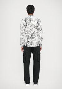 Pantaloni cargo neri abbinati a una camicia a maniche lunghe con un motivo vorticoso bianco e grigio. La camicia ha un colletto classico e polsini con bottoni.