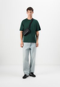 Zelené tričko s kulatým výstřihem, světle modré džíny rovného střihu, černá krosová taška na rameno s popruhem a černé tenisky. Jednoduchý design, uvolněný střih.