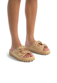 Sandales à glissière beiges avec deux brides réglables, ornées de clous dorés, et une semelle épaisse et texturée pour une meilleure adhérence.