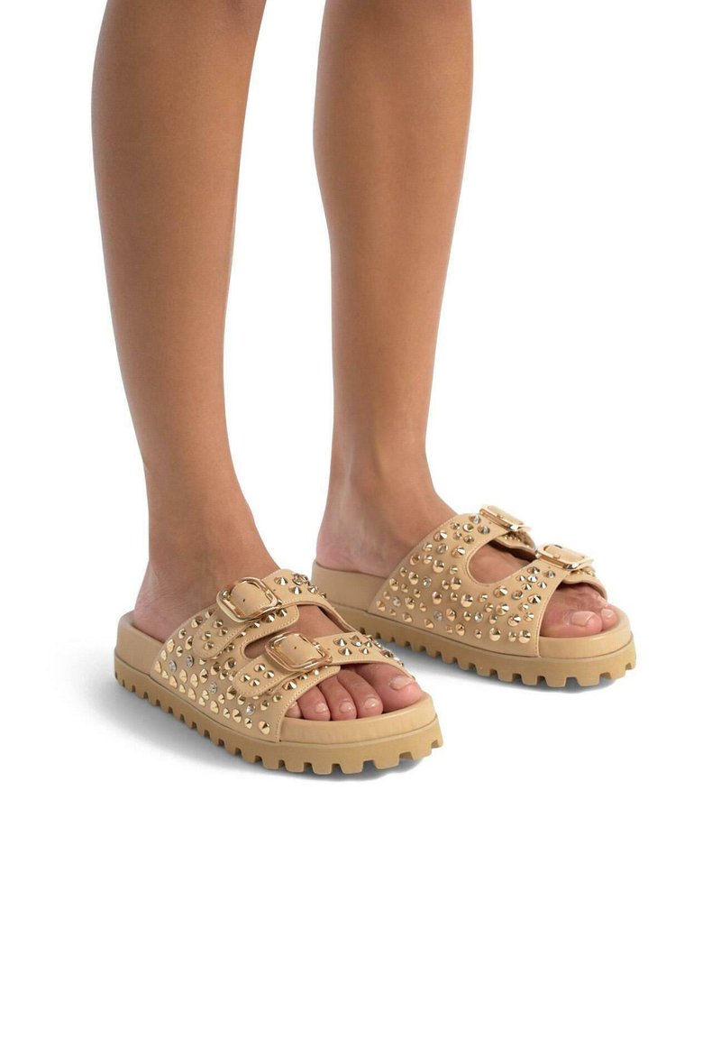Sandales à glissière beiges avec deux brides réglables, ornées de clous dorés, et une semelle épaisse et texturée pour une meilleure adhérence.