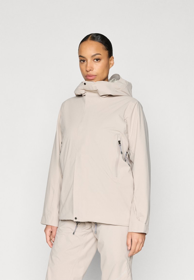 Jachetă impermeabilă bej cu guler înalt, glugă reglabilă și buzunare cu fermoar. Textură netedă și croială dreaptă.