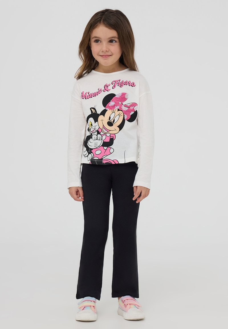 Maglietta bianca a maniche lunghe per bambini con una grafica di Minnie Mouse e Figaro, abbinata a pantaloni neri a zampa d'elefante e scarpe da ginnastica colorate.