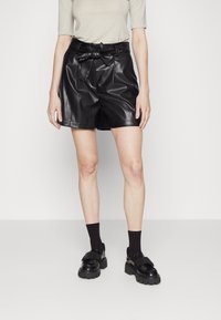 Czarne krótkie spodenki ze skóry z paskiem w talii, o gładkiej fakturze i luźnym kroju, połączone z czarnymi skarpetkami i masywnymi czarnymi butami.