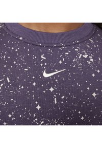Ljubičasti dukserica s bijelim pjegama i uzorkom nalik na zvijezde, s malim izvezenim Nike logom na grudima i rebrastim izrezom.