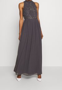 Grå lång klänning med halterneck, dekorerad bodice med pärlbroderi och en flödande chiffongkjol. Stylad med vita klackar.