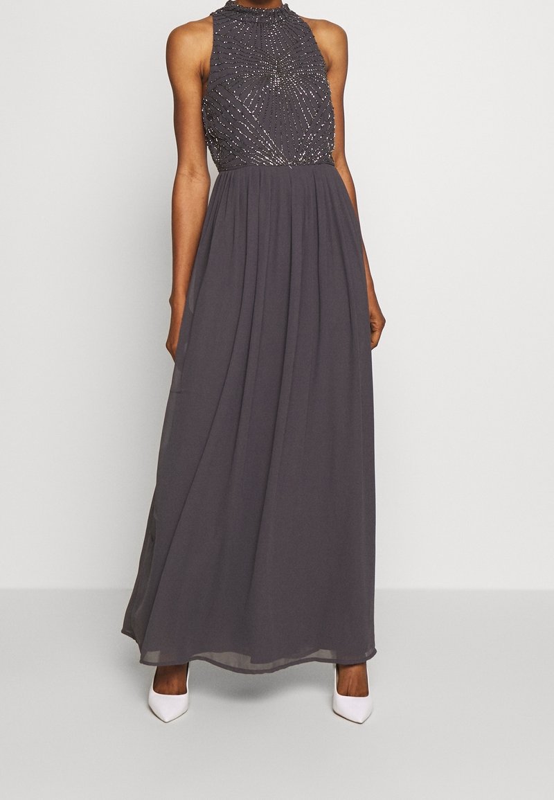 Grå lång klänning med halterneck, dekorerad bodice med pärlbroderi och en flödande chiffongkjol. Stylad med vita klackar.
