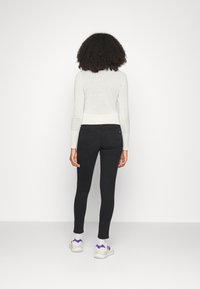Jeans skinny negros combinados con un suéter ajustado claro. El conjunto incluye zapatillas blancas con acentos morados, vistas desde la parte trasera.