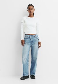 Bela dolgi rokav, krojena majica v kombinaciji s svetlo modrimi ravno krojenimi jeans hlačami. Nizkonasprotno šivanje in klasičen gumbni sprednji del.