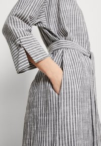 Grau-weiße gestreifte Robe mit dreiviertel Ärmel, einem Wickelgürtel und einer Seitentasche aus strukturiertem Stoff.