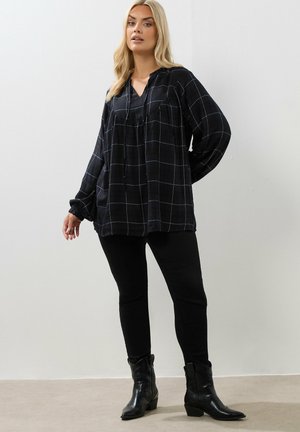 Blusa a maniche lunghe bianco e nero a scacchi con scollatura a V e dettagli arricciati, abbinata a pantaloni neri aderenti e stivaletti neri alla caviglia.