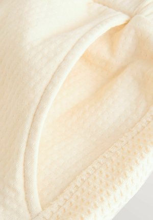 Tissu couleur crème avec une surface texturée, présentant un bord lisse et un détail tissé d'un côté. Matériau doux et léger.