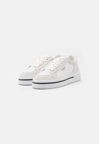 Baskets blanches en mélange de cuir et de daim, présentant des détails perforés, des lacets plats et une semelle plateforme texturée avec une rayure noire.