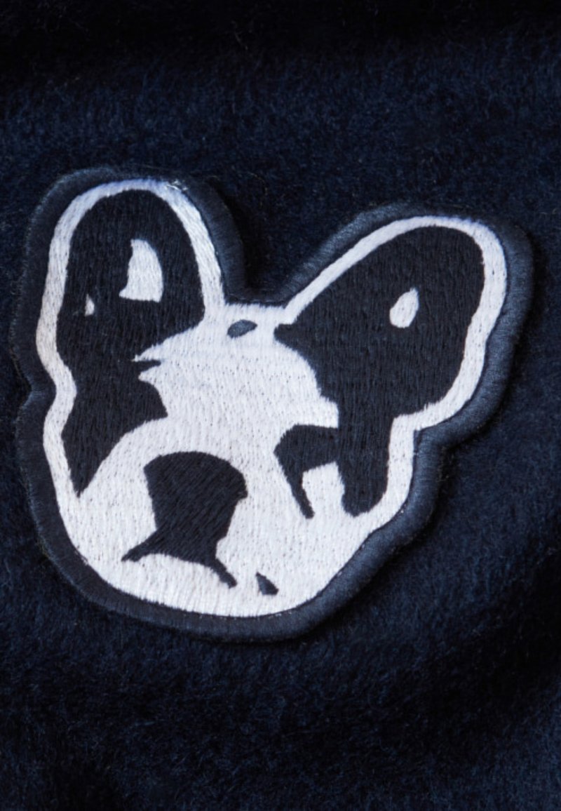 Patch brodé en noir et blanc représentant un visage d'ours sur un fond marine, avec des caractéristiques faciales distinctes et une texture douce.