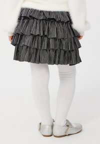 Gonna ruffled a strisce nere e grigie con design a strati, abbinata a collant bianchi e scarpe argento glitterate con cinturini alla caviglia.