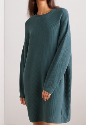 Abito lavorato a coste in teal con maniche lunghe, vestibilità comoda e spacchi laterali. La struttura è morbida e uniformemente distribuita, aumentando il suo calore.