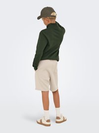 Grønt fleece pullover, beige shorts, hvide sokker og beige sneakers med brune accenter, set bagfra mod en neutral baggrund.
